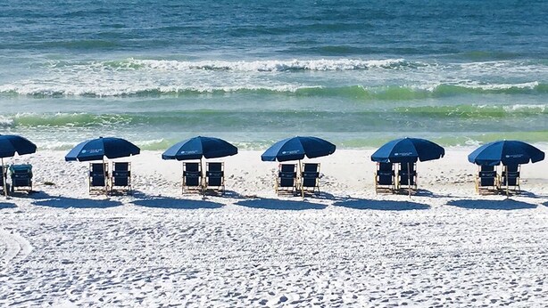Una playa con hileras de sombrillas azules y sillas de playa.