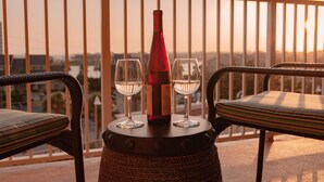 Un balcón con sillones de mimbre y una mesa con una botella y dos vasos.