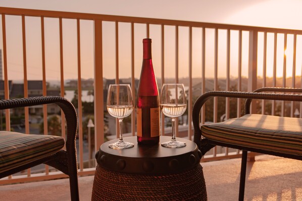 A balcony with wicker chairs and a table holding a bottle and two glasses.