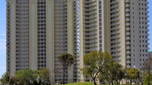 Un edificio residencial alto con varios balcones, rodeado de un área verde bien cuidada con árboles.