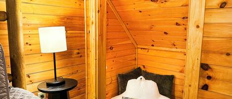 Une pièce chaleureuse avec des murs en bois, un lit, une petite table avec une lampe et un coussin sur une chaise.