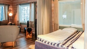 Una habitación acogedora de estilo cabaña, con una cama, una silla, una lámpara y una ventana con cortinas.