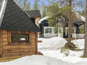 Una cabaña de madera con techo hexagonal, rodeada de nieve y árboles.