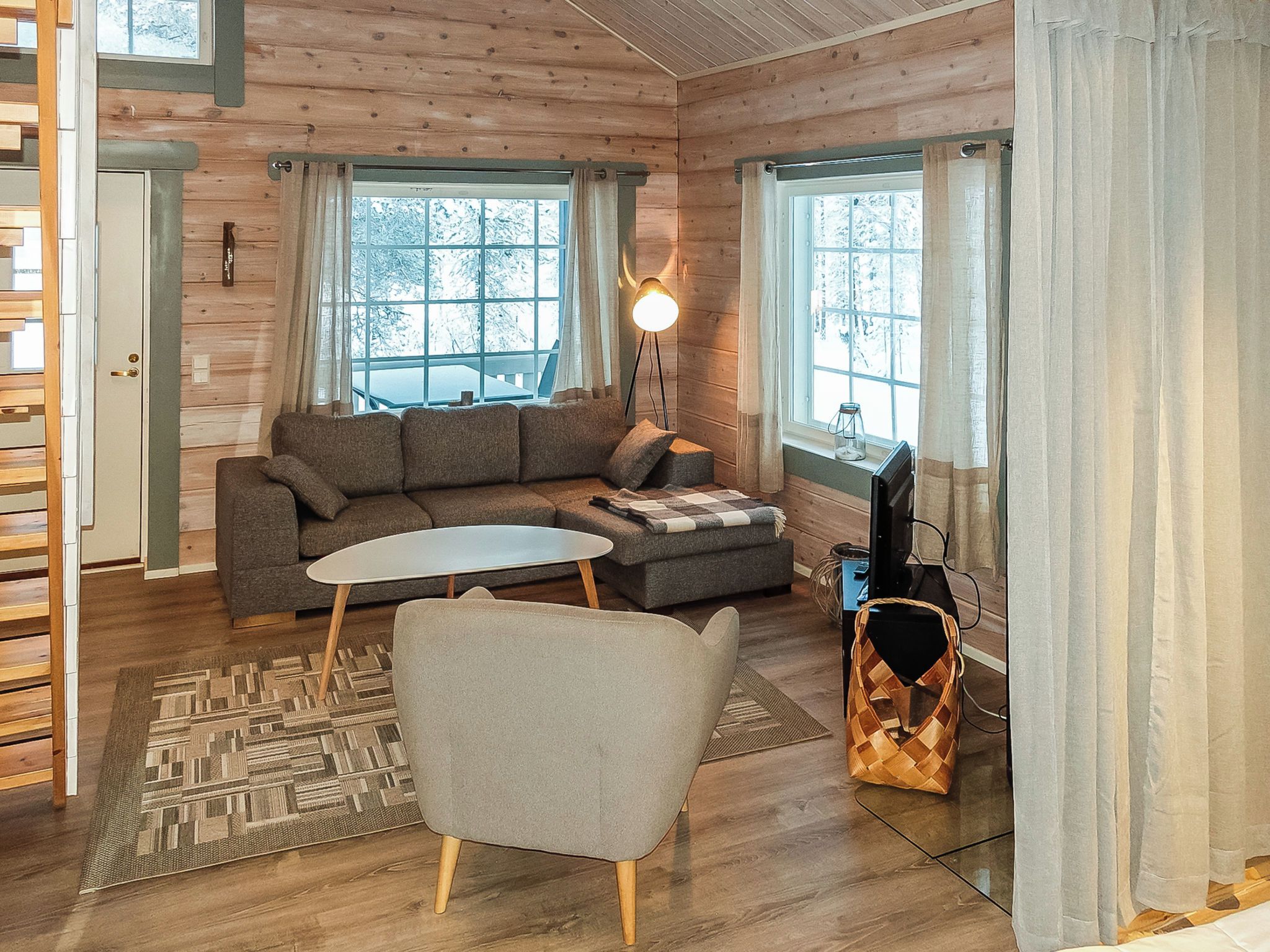 A cozy cabin interior with a sofa, a small table, a chair, a lamp, and a television.