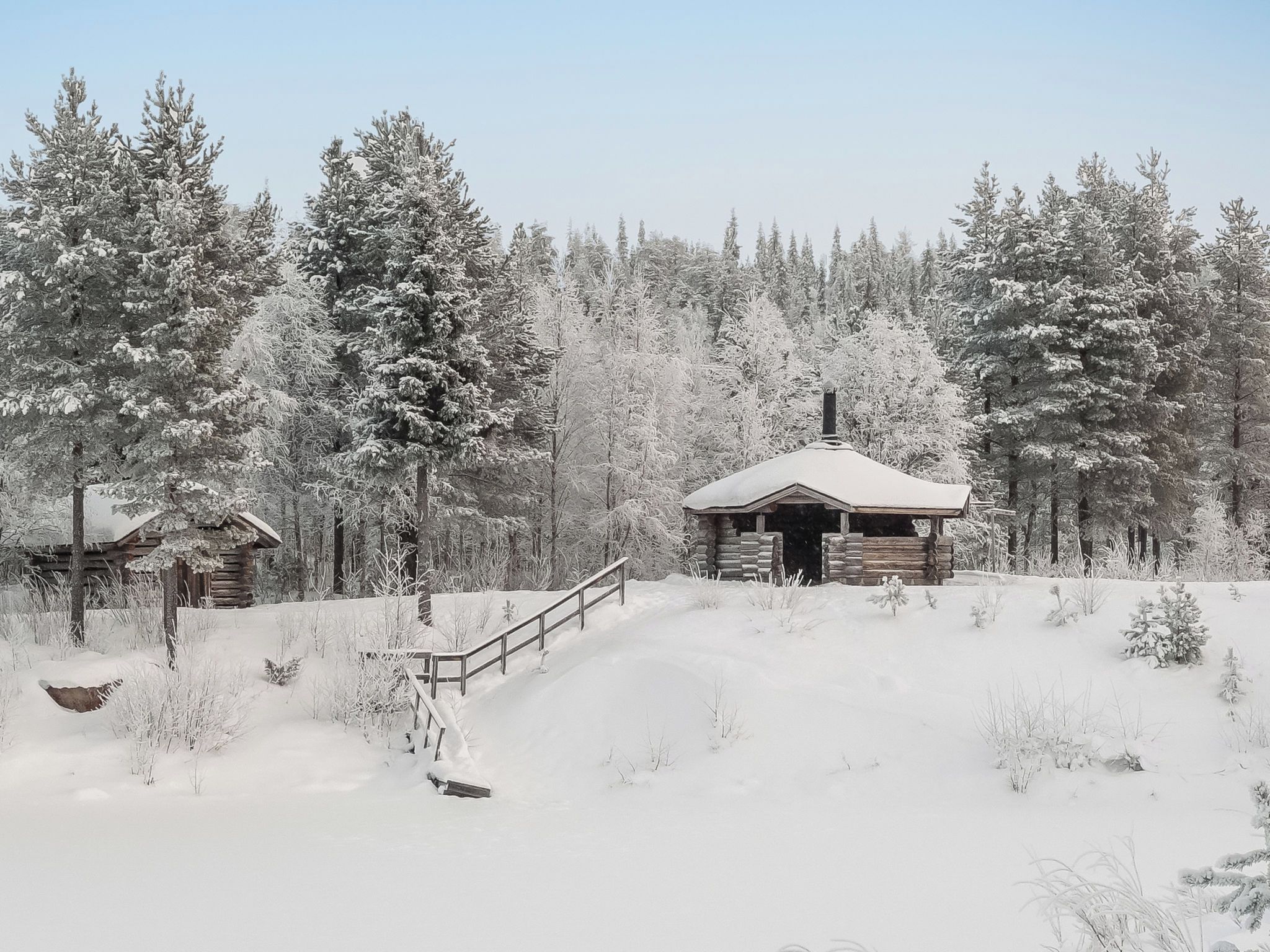 A log cabin with a snow-covered roof, surrounded by a forest.