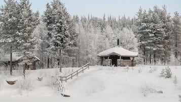 A log cabin with a snow-covered roof, surrounded by a forest.