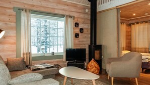 Un salón acogedor con sofá, sillón y televisor. Se ve una chimenea al fondo.