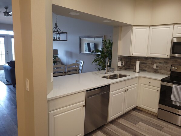 A modern kitchen with white cabinets, stainless steel appliances, and a wooden floor.