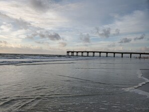 A pier extending into the sea with waves lapping at the shore.