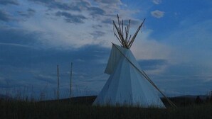A tipi in a grassy field under a night sky with a visible moon. - Bird Lodge Tipi at Stepping Stone (Bigfork)
