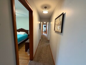 A narrow hallway with a carpeted floor, wooden door frame, and a bed with a blue bedspread.