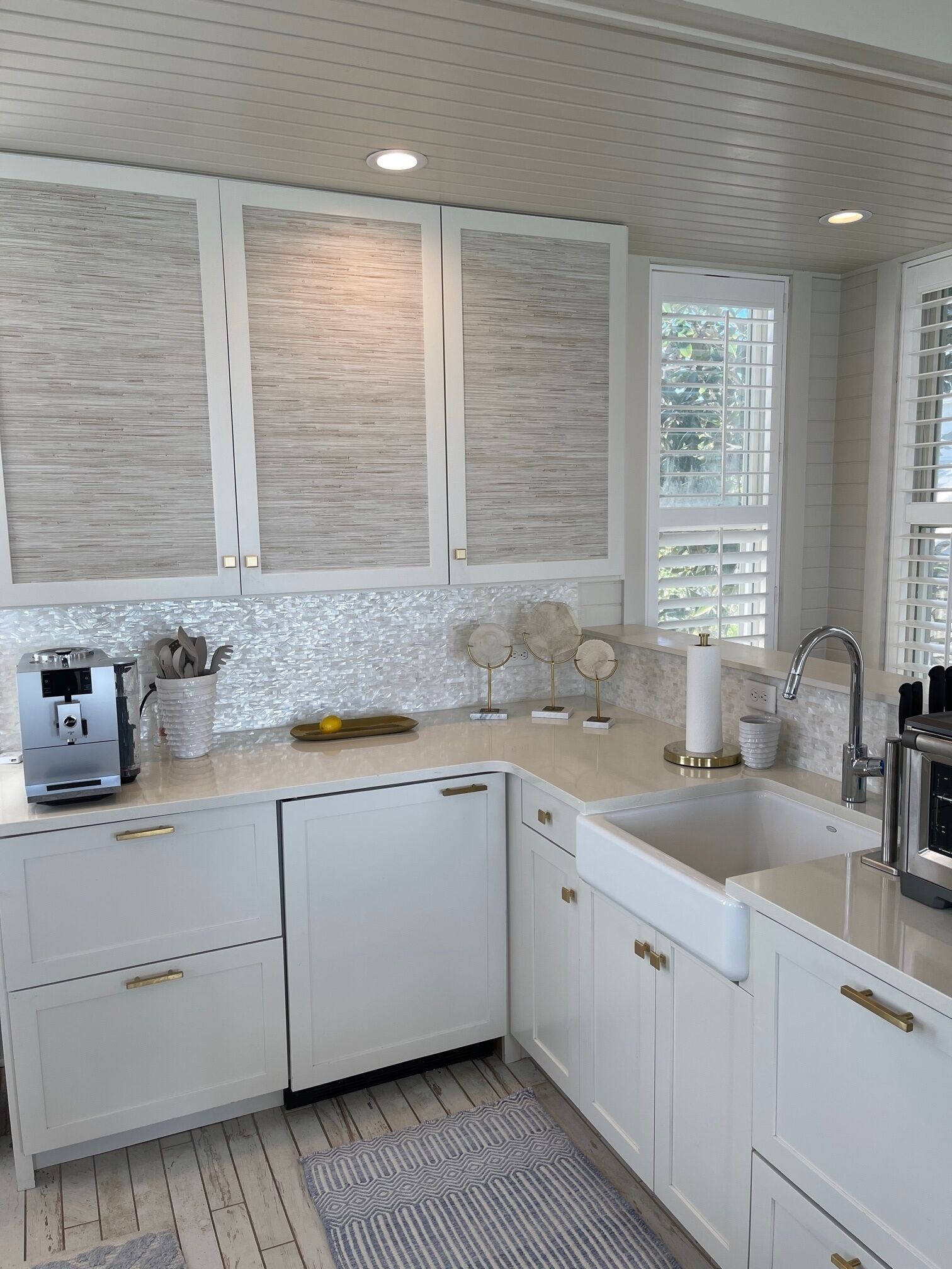 A modern kitchen with white cabinetry, a built-in dishwasher, a sink, and a window with blinds.