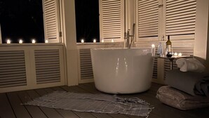 Una terraza de madera con una bañera independiente, velas y una toalla.