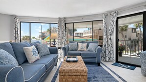 A modern living room with two sofas, a coffee table, and large windows offering a view of the outside.
