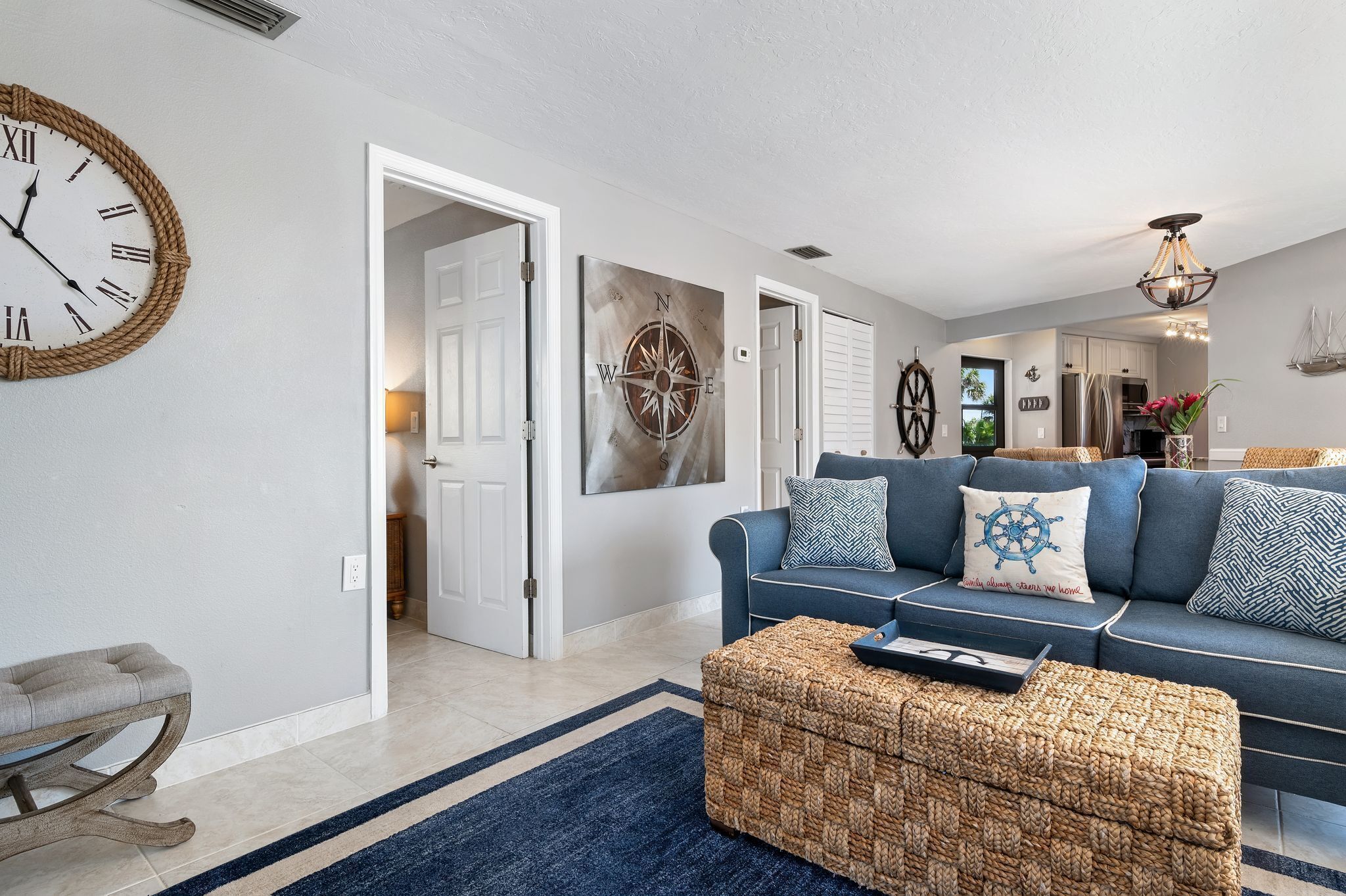 A living room with a blue sofa, a woven ottoman, and a wall clock.