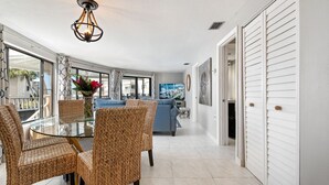 A modern living room with a glass dining table, wicker chairs, a blue sofa, and a television.