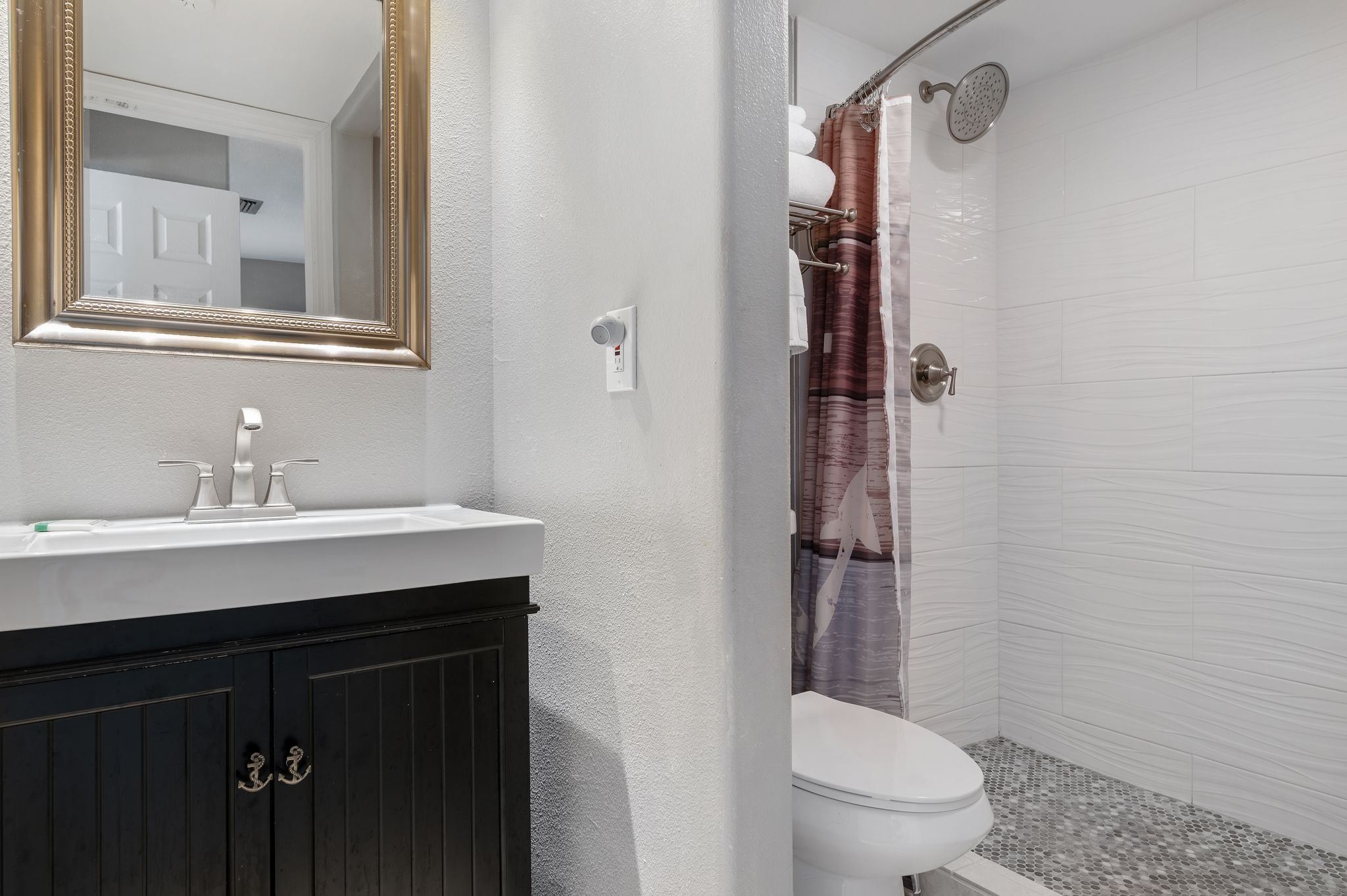 Een badkamer met een witte wastafel, een donkere kast en een douche met een gestreept gordijn.