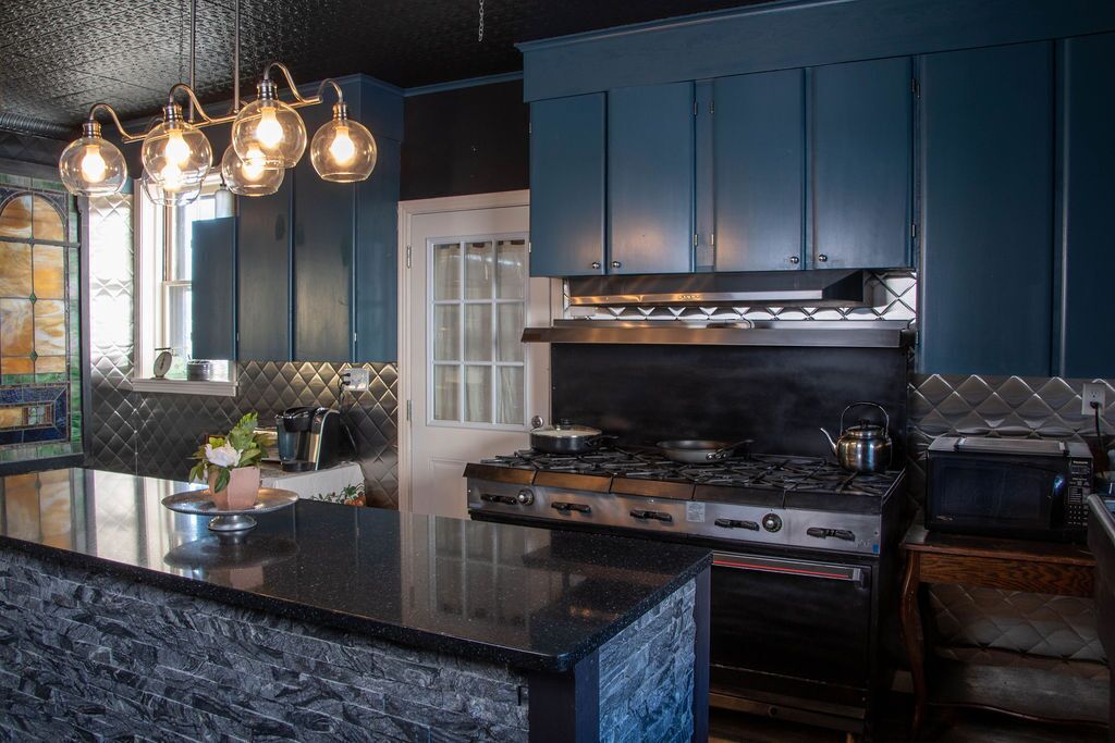 A modern kitchen with dark blue cabinets, a central island with a stove, and pendant lighting.