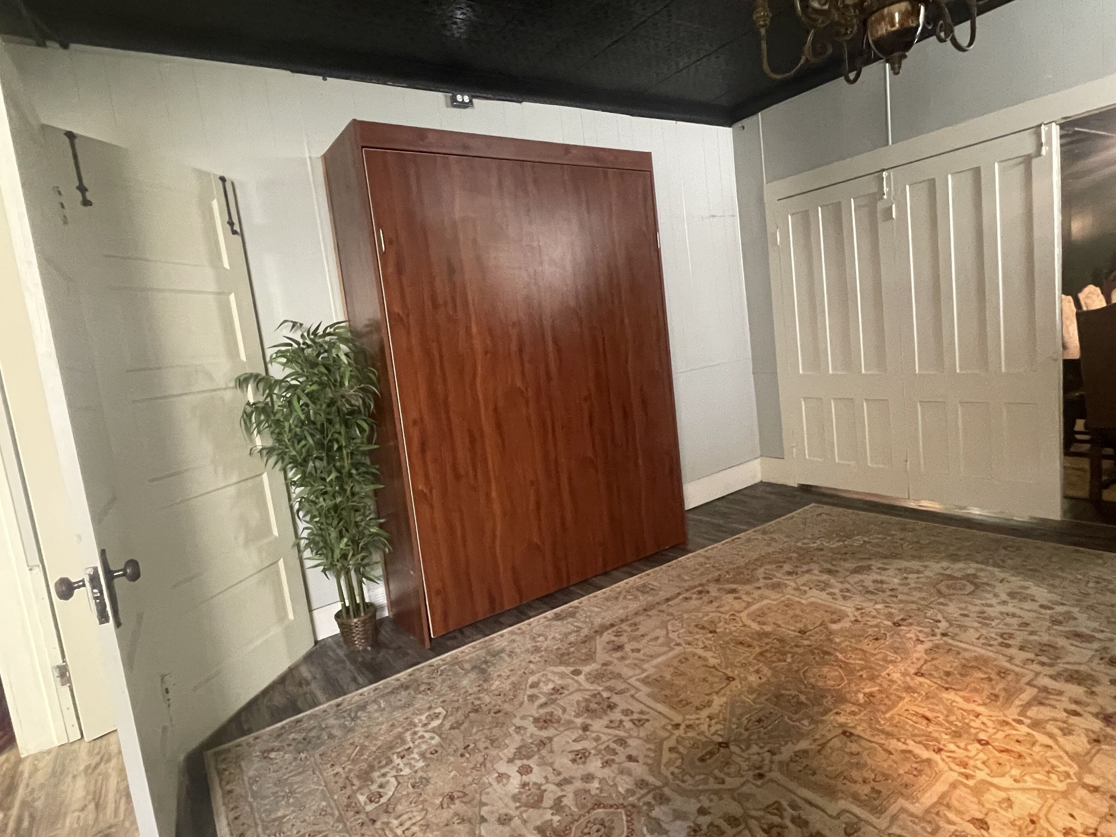 A room with a large wooden wardrobe, a patterned rug, and a potted plant.
