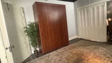 A room with a large wooden wardrobe, a patterned rug, and a potted plant.