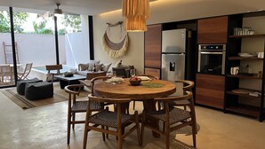 A modern kitchen with a round wooden dining table, wicker chairs, and a hanging light fixture. - Apartment With Private Plunge Pool - Ground Floor by Sessile (Tulum)