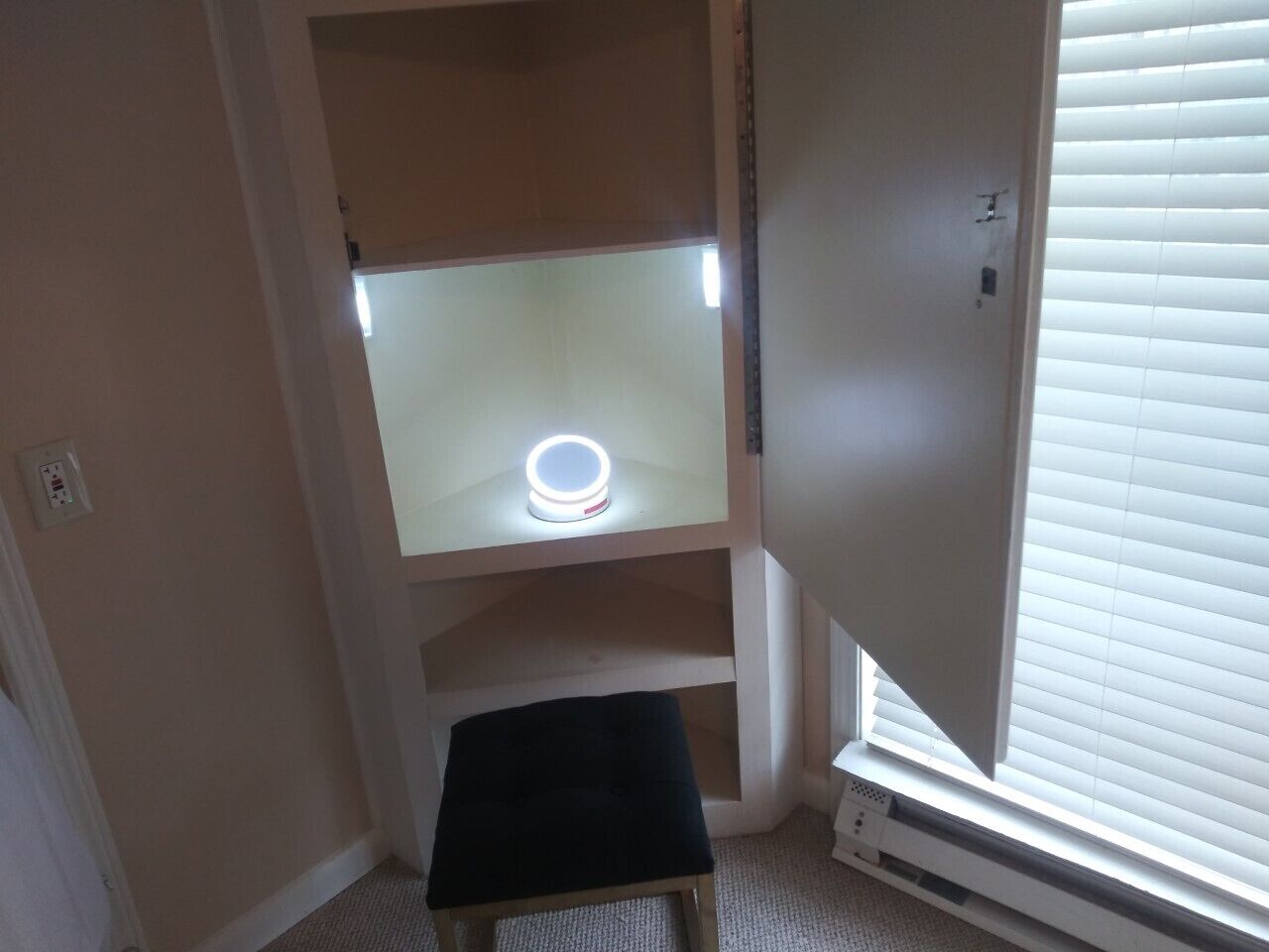 Ein Eckzimmer mit eingebauter Bank, einem Regal mit Lampe und einem Fenster mit Jalousien.