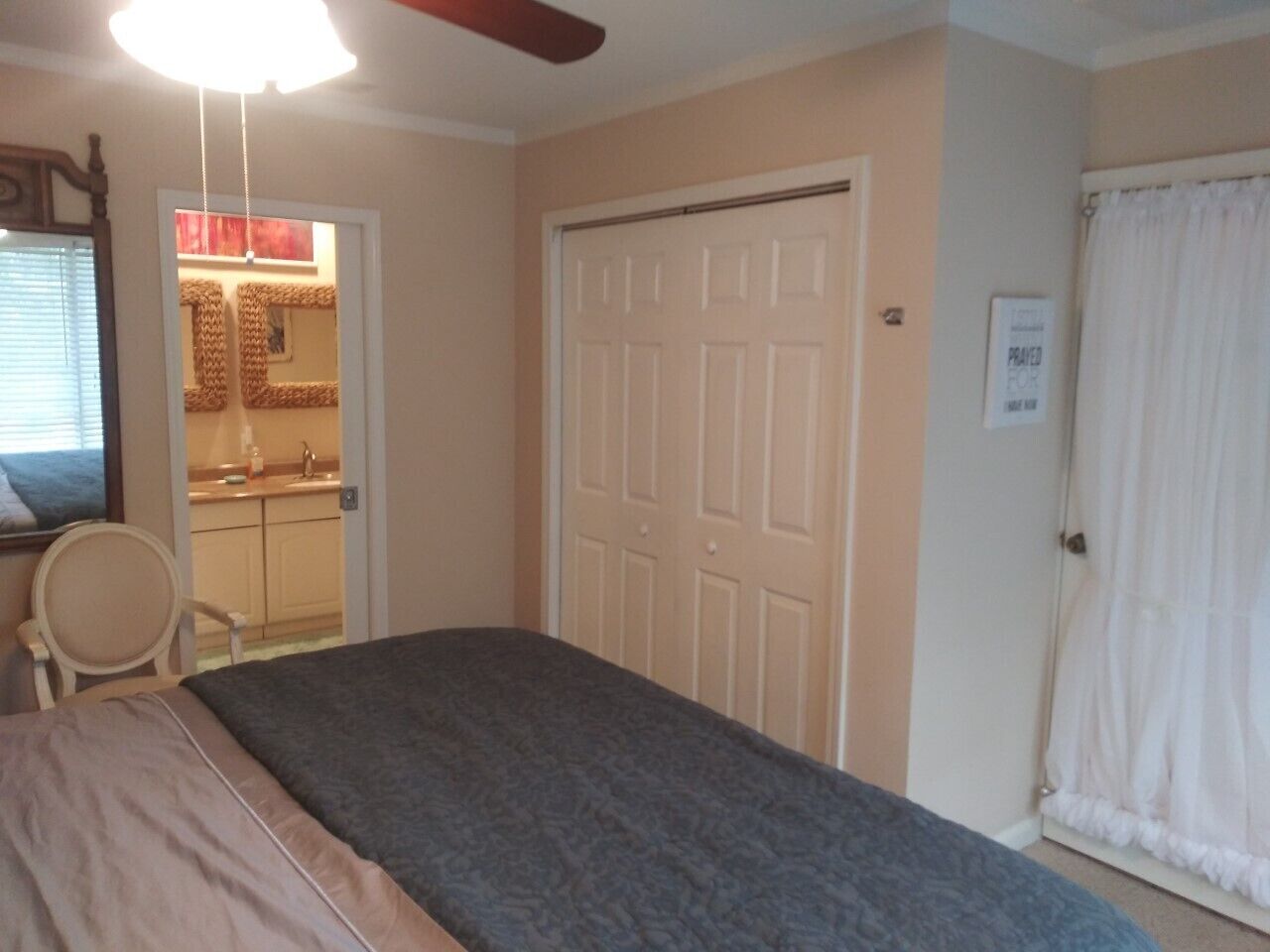 Une chambre à coucher avec un lit, une porte, une chaise et un espace salle de bain visible.