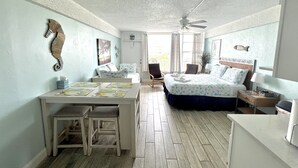 Ein Zimmer mit einem Bett, einem Schreibtisch und einem Stuhl. Ein Fenster mit Vorhängen bietet einen Blick ins Freie.