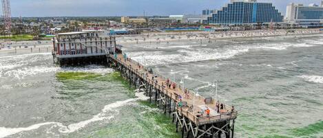 A pier extending into the ocean with a view of the beach and city buildings in the background.