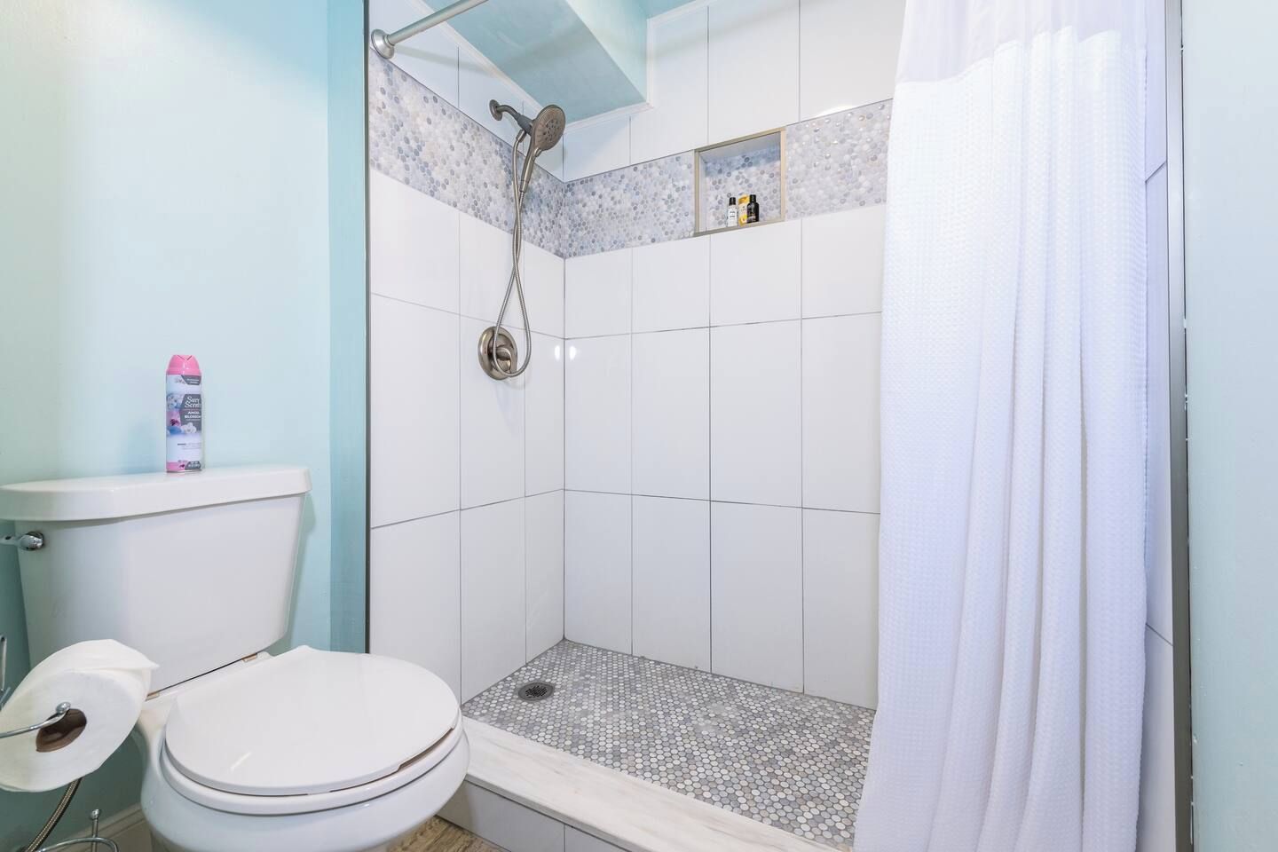 Een badkamer met een douche, toilet en een plank met toiletartikelen.