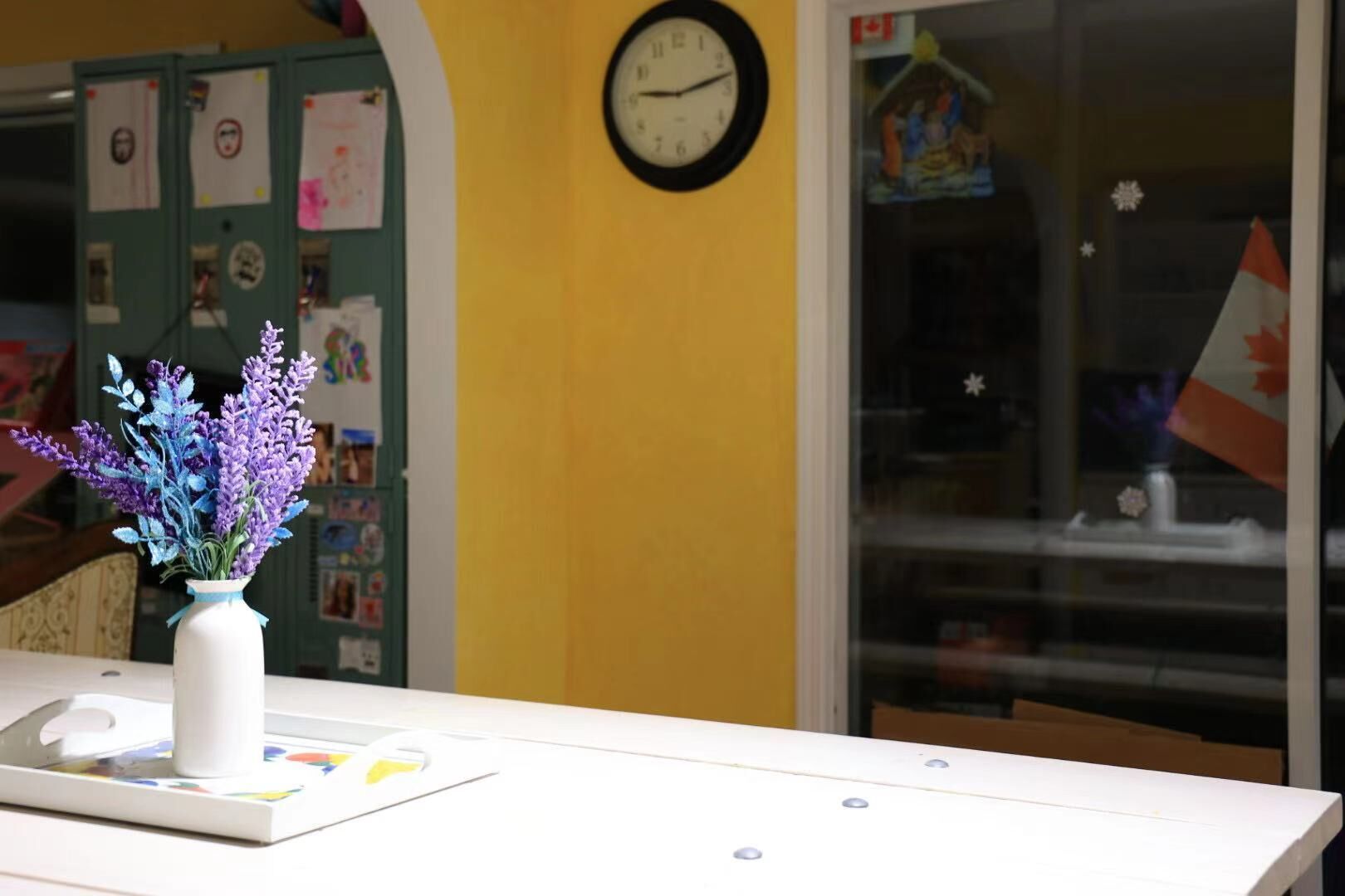A reception desk with a clock, a vase of purple flowers, and a bulletin board with various notices.