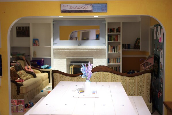 Un coin repas avec une table blanche, un centre de table floral et une vue sur un salon comprenant un canapé et une cheminée.