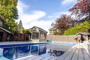 Un jardin avec une piscine, une terrasse en bois et un espace patio couvert.