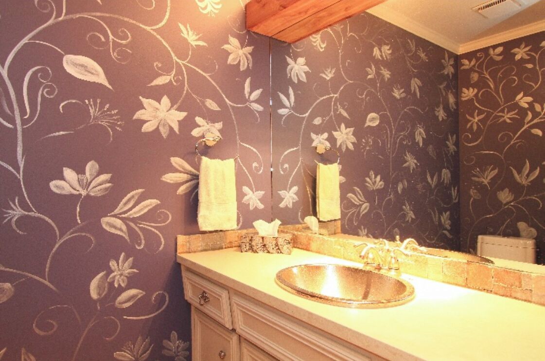A bathroom with a floral wallpaper, a round sink, and a mirror above it.