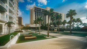Um pátio de hotel com palmeiras, piscina e um edifício grande com vários andares.