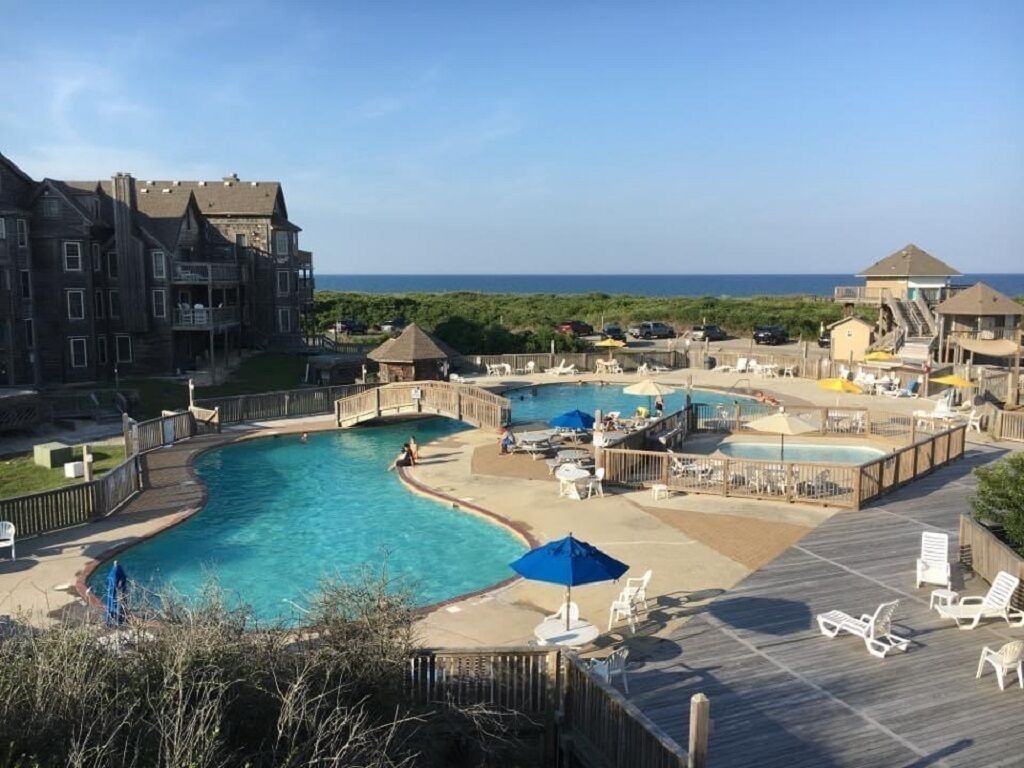 A resort with multiple swimming pools, a wooden deck, and a view of the ocean.