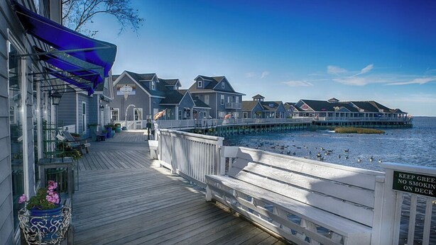 A wooden pier extending into a body of water with a row of houses on the other side. - BIS-Duck - 2BR/2BA - First Floor, Great Beach and Pools! (Duck)