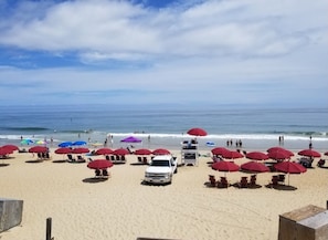 A beach with red umbrellas, a white truck, and a lifeguard tower.