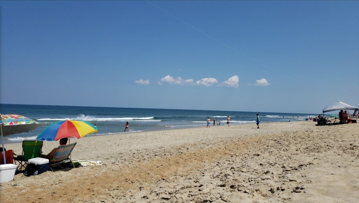 A beach with a clear sky, footprints in the sand, and a colorful umbrella.