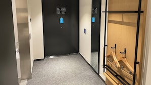 A hallway with a black elevator door, a blue wheelchair accessibility sign, and a wooden wardrobe with metal hangers.