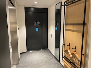 A hallway with a black elevator door, a blue wheelchair accessibility sign, and a wooden wardrobe with metal hangers. - Henn na Hotel Seoul Myeongdong (Seoul)