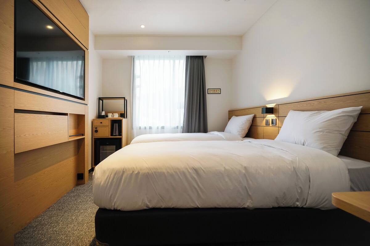A hotel room with a bed, a TV, a desk, and a window with curtains.