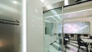 A modern restaurant with a glass partition, a large screen displaying space imagery, and a seating area with tables and chairs.
