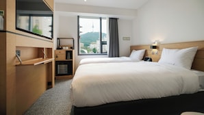 A hotel room with a bed, a desk, a TV, and a window with a city view.