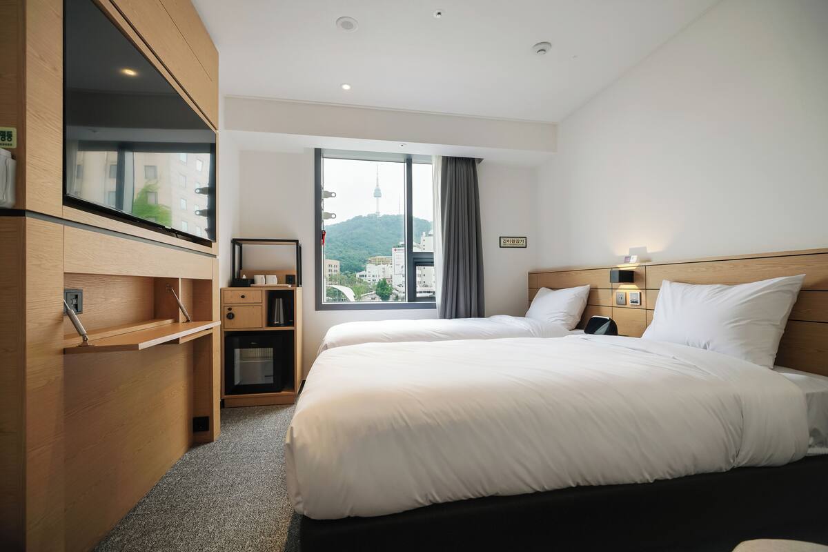 A hotel room with a bed, a desk, a TV, and a window with a city view.
