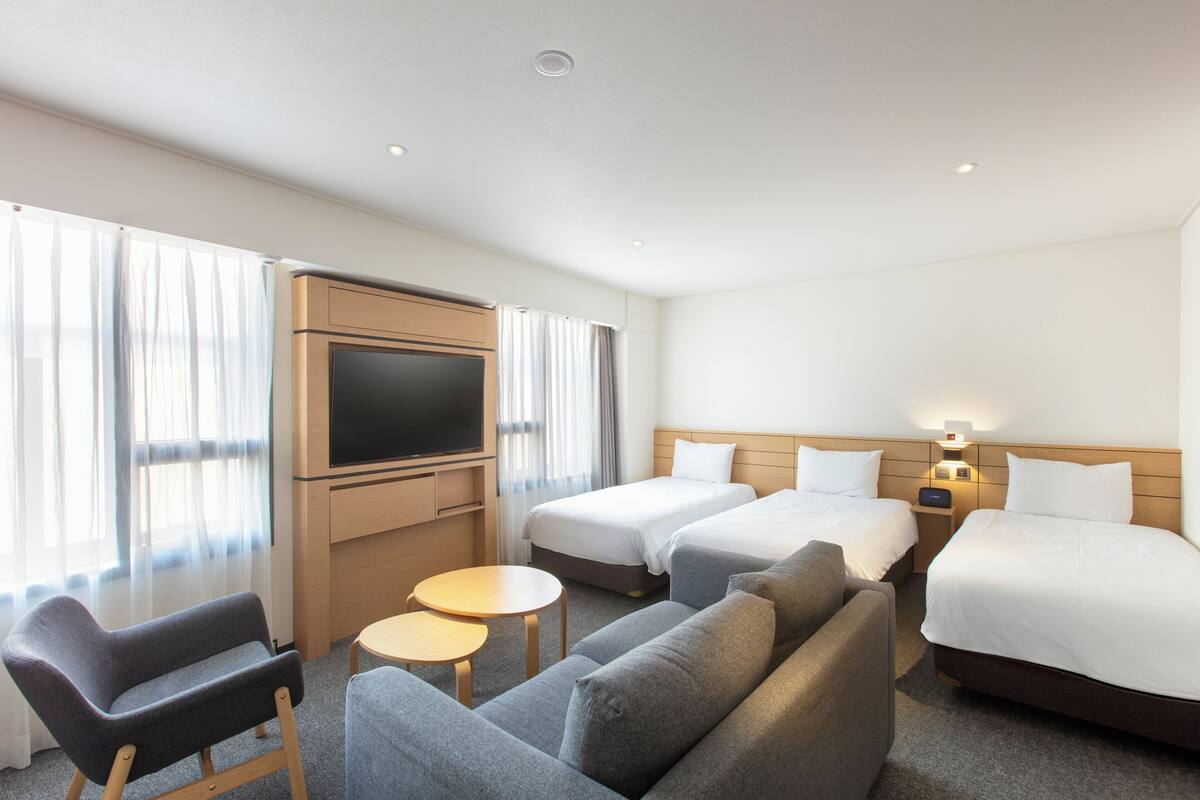 A hotel room with two beds, a sofa, a TV, and a small table.