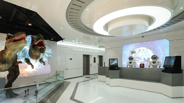 A modern hotel lobby with a glass railing, a reception desk, and a digital display.
