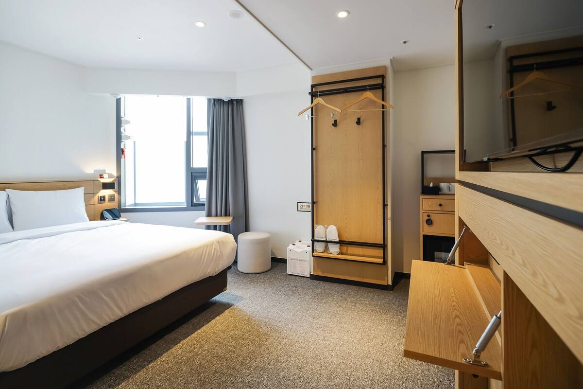 A hotel room with a bed, a wardrobe, a small table, a mirror, and a TV.