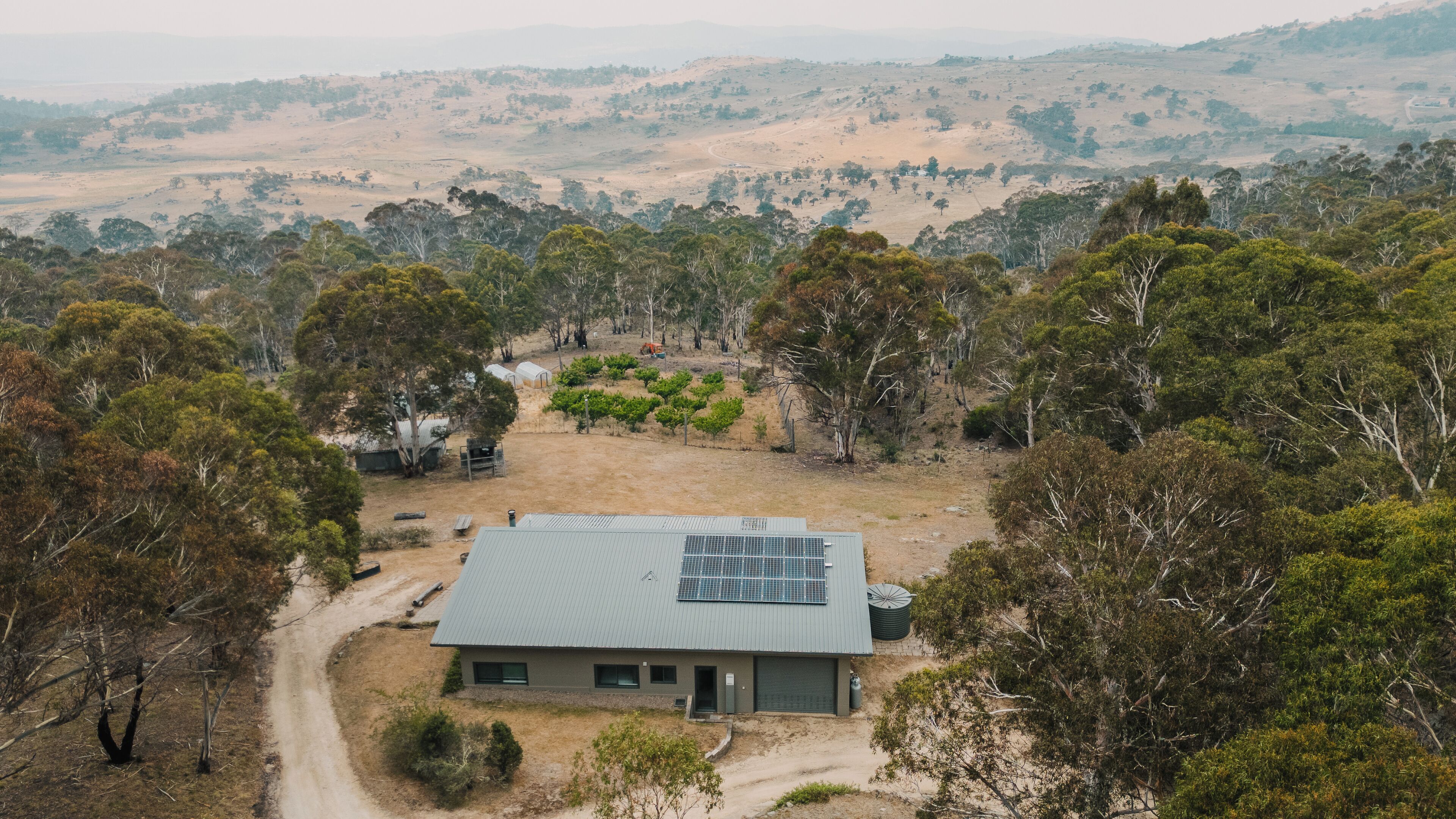 Une maison dotée d’un toit recouvert de panneaux solaires, entourée d’arbres et située dans un paysage vallonné.