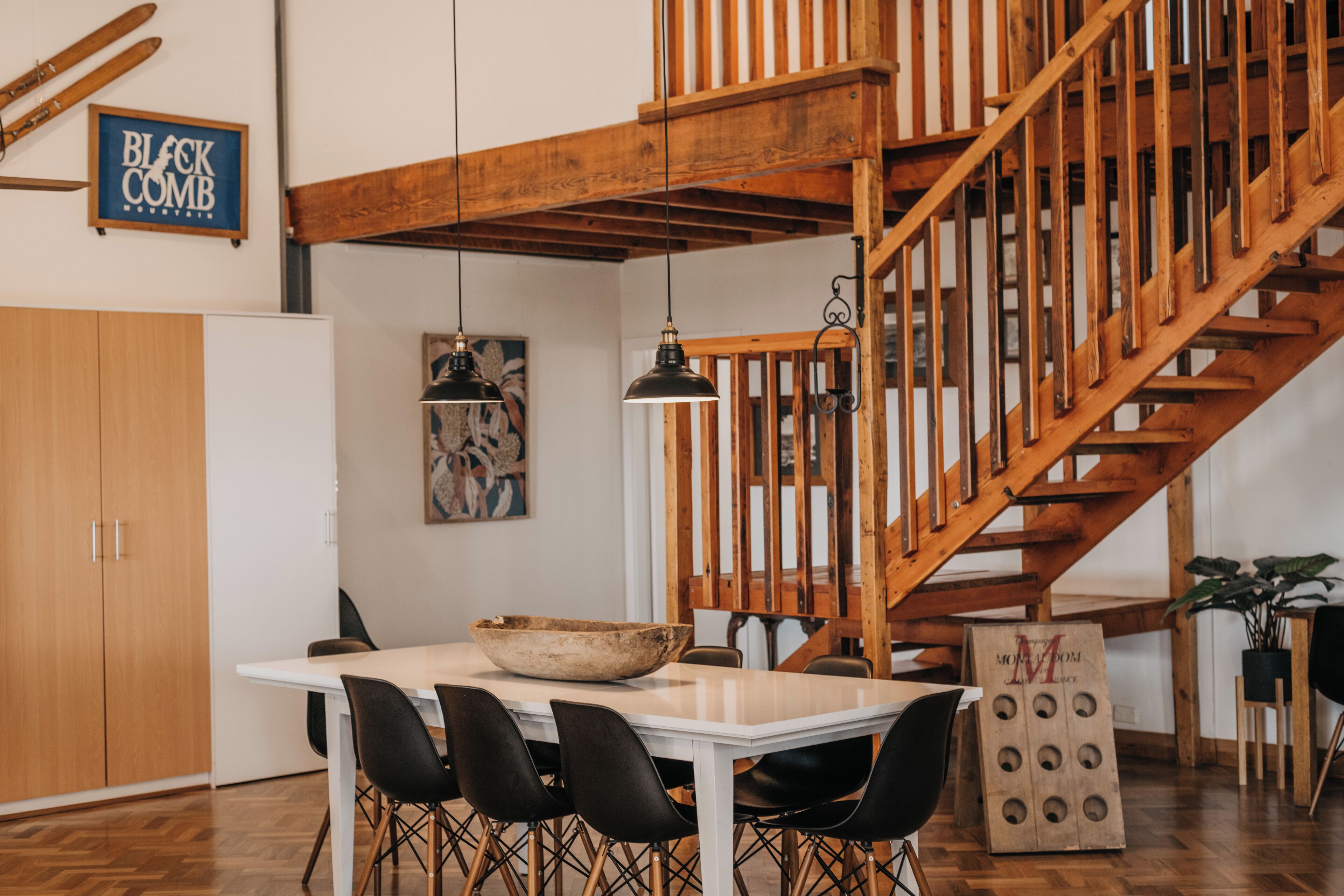 A dining area with a white table, black chairs, and a wooden staircase.
